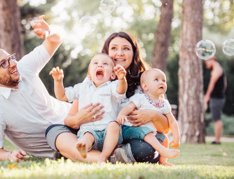 Joyful family enjoying a sunny day in the park while playing with bubbles.